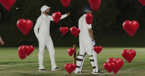 Fielder pointing while batsman standing amid floating red hearts on night cricket ground