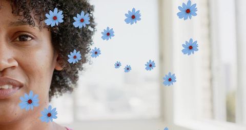 Smiling woman with short curls posing by sunlit window with blue daisy overlays close-up headshot