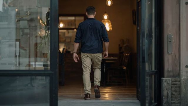 Man walking into cozy cafe through glass doors wearing navy shirt and khaki pants