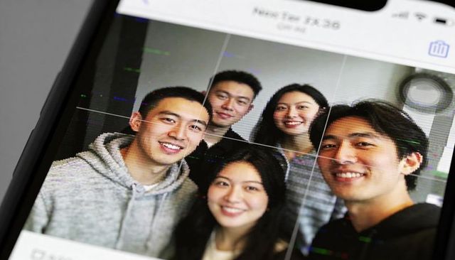 Asian young professionals smiling for smartphone selfie in modern office with grid overlay
