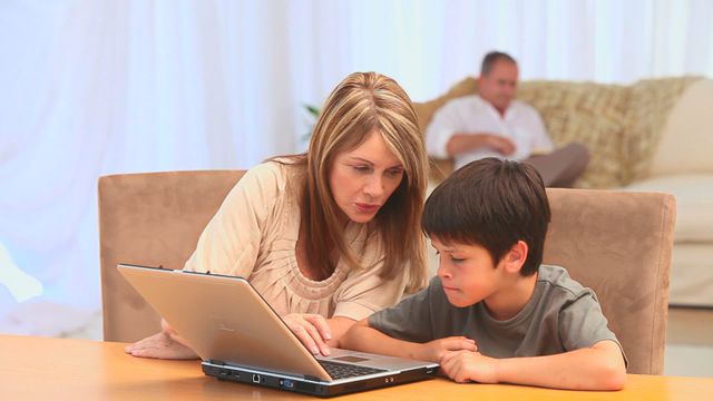 Grandmother and grandson sitting at a table in the living room focusing on a laptop. This scene of intergenerational bonding is ideal for ads, articles, and social media posts emphasizing technology education in families, the importance of spent time together, and learning from elders.