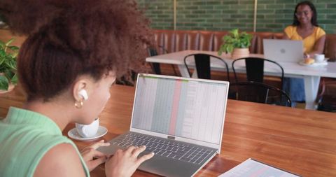 African american women working in cafe typing spreadsheet on laptop for productivity