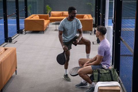 Padel players chatting in modern club lounge holding paddles and duffel bag