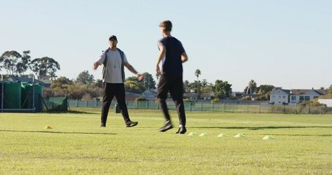 Coach leading teenage players through cone agility drills on suburban sports field