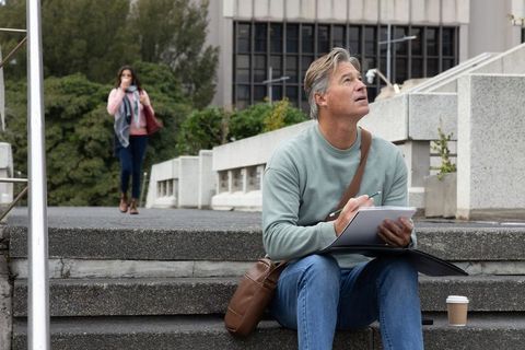 Middle-aged man sketching city architecture on steps with coffee and messenger bag