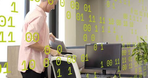 Older professional placing laptop on office chair at cubicle desk with binary code overlay