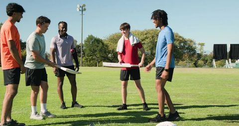 Teenage players practicing cricket drill on sunny sports field with bats and ball