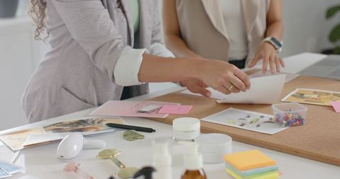Two women arranging mood board on corkboard in creative studio collaborating on layout