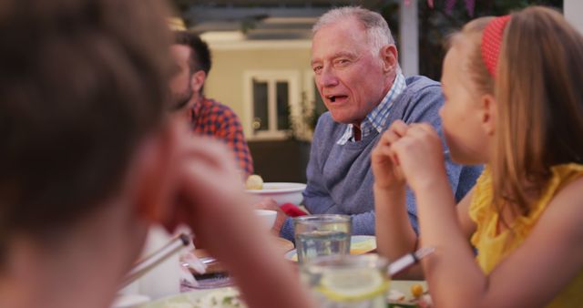 Caucasian grandfather talking to grandchildren at family dinner table in garden - Download Free Stock Photos Pikwizard.com