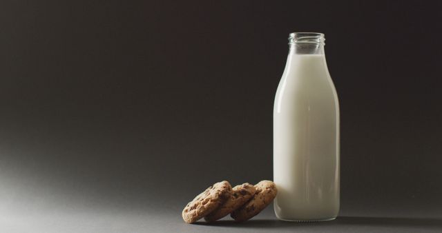 Bottled milk and chocolate chip cookies resting against dark background. Ideal for advertising dairy products, promoting healthy snacks, illustrating cooking and baking materials, or use in food and beverage blogs.
