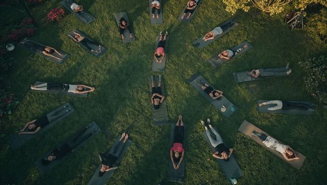 Outdoor group yoga practicing relaxation on green lawn with mats and water bottles