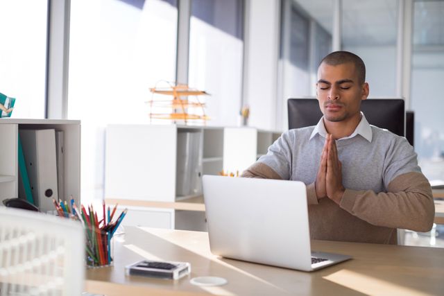 Male executive practicing yoga at his office desk, promoting mindfulness and relaxation in the workplace. Ideal for illustrating concepts of workplace wellness, stress relief, and mental health in a professional setting. Useful for articles, blogs, and presentations on corporate wellness programs and productivity tips.
