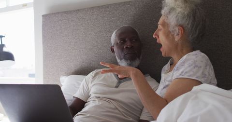 Senior Couple Relaxing with Laptop in Cozy Bedroom Setting