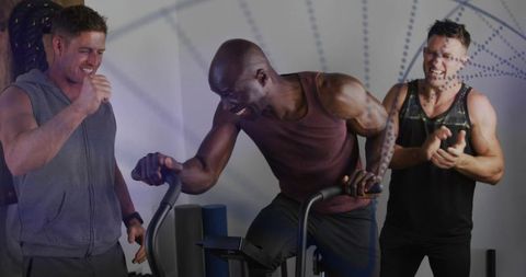 Power pedaling workout: man pushing hard on stationary bike while teammates cheering