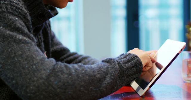 Person in a cozy casual sweater using a tablet indoors, emphasizing modern technology and casual comfort. Useful for illustrating tech usage in everyday life, digital interaction, and home or office settings.