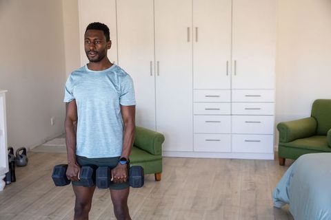 African american man lifting dumbbells in modern bedroom home workout