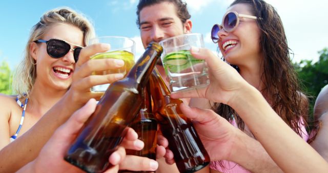 Group of friends clinking their drinks while enjoying a summer outdoor party. People are smiling and having fun, making this perfect for use in content related to celebration, friendship, summer activities, outdoor parties, and social gatherings.