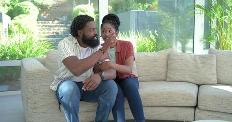 African couple relaxing on beige sectional sofa in sunlit modern living room