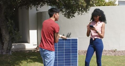 Black woman and asian man holding solar panel while checking phone, planning home solar