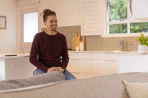 Smiling man sitting on kitchen stool drinking coffee in bright modern open-plan home