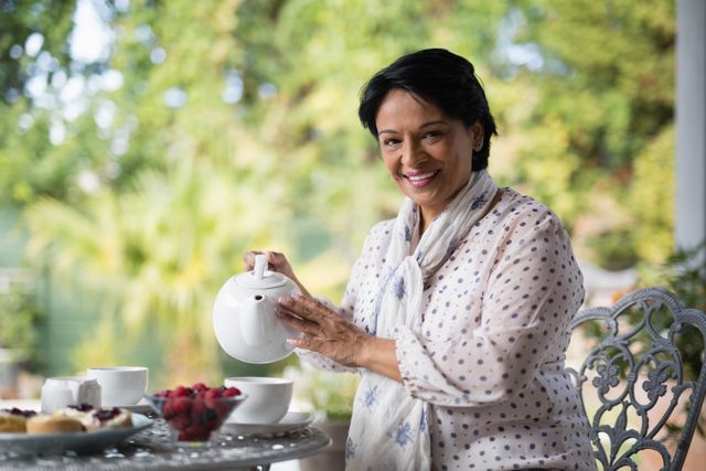 Mature woman enjoying a relaxing tea time outdoors, pouring tea into a cup on a garden patio. Ideal for use in lifestyle blogs, senior living advertisements, and content promoting relaxation and leisure activities.