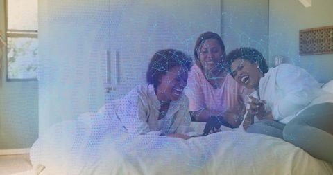 Laughing friends lounging on bed sharing smartphone, cozy loungewear, relaxed morning