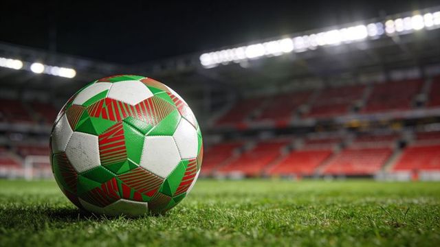 Soccer ball gleaming on stadium turf under floodlights, resting in foreground at night
