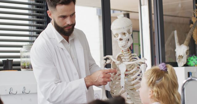 Male teacher focusing on human skeleton model while curious students attentively listening in classroom. Ideal for educational materials, science textbooks, school websites, and content highlighting interactive teaching methods, anatomy classes, or biology lessons.