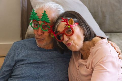 Senior couple with festive glasses puckering lips on cozy sofa