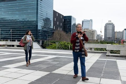 Senior man walking and woman talking on phone on modern urban plaza with city skyline