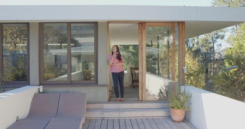 Asian Woman Relaxing on Modern Wooden Deck with Smartphone and Coffee