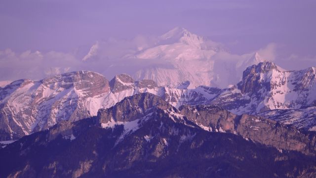 Snow-capped mountains with hues of purple in the early morning light provide a breathtaking view. Perfect for use in travel blogs, nature documentaries, or inspirational posters depicting the grandeur of the natural world.