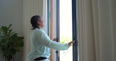 African american woman opening sliding glass door and drawing curtains in modern home