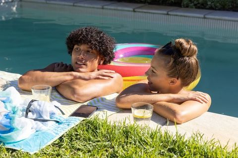 Young couple relaxing and chatting at pool edge with colorful float and lemonade