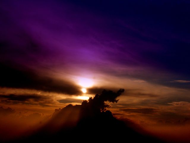 This visually rich scene captures a dramatic sunset with vibrant purple and orange hues in the sky. Sun rays peek through dark clouds, creating a striking contrast. Perfect for use in inspirational and nature-themed content, backgrounds, or artistic projects aiming to evoke emotion and awe.