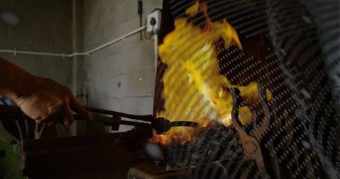 Blacksmith forging glowing metal with tongs amid fiery forge flames and sparks