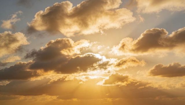 Sunbeams breaking through golden cumulus clouds, warm horizon glow at sunset