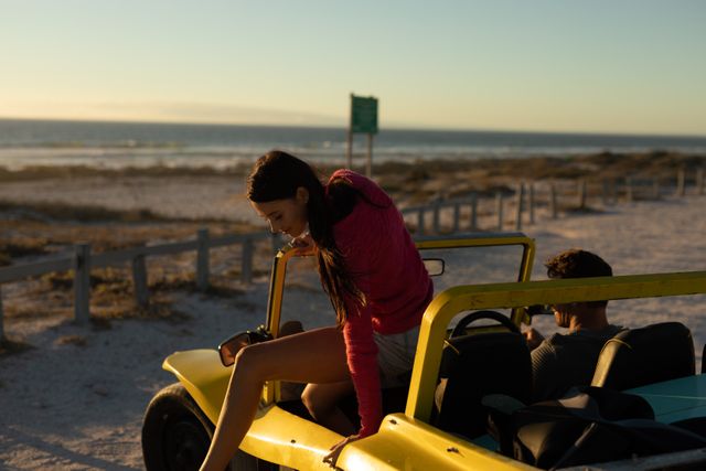 Happy caucasian couple in beach buggy by sea at sunset, woman climbing out. beach stop off on romantic summer holiday road trip.