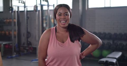 Confident plus-size african american woman smiling at gym in pink tank top