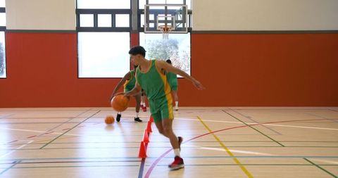 Diverse basketball players dribbling around cones in gym