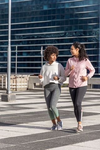 Multicultural women walking and talking in sunlit urban plaza wearing athleisure sneakers
