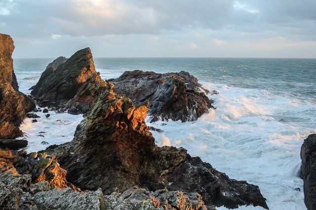 Shows waves crashing on rocky cliffs during sunrise, creating a dramatic coastal scene. Perfect for use in travel brochures, coastal themed settings, nature magazines, and websites focusing on marine environments. Offers a feel of nature's raw power and beauty.