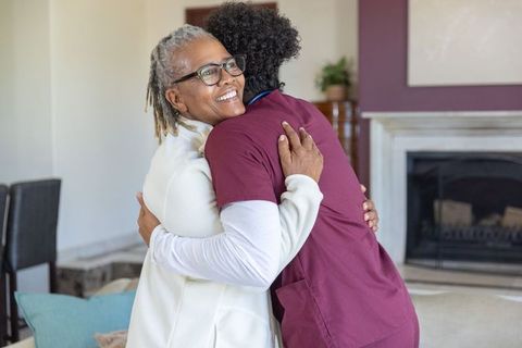 African american senior woman hugging caregiver in home healthcare visit showing warmth