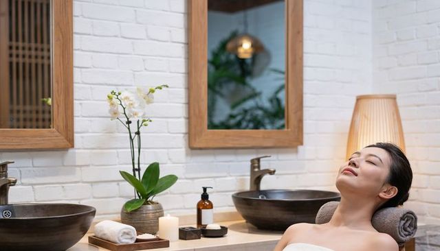 Reclining woman relaxing in serene spa with orchid, stone sinks and ambient lighting