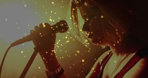 Teen singer leaning into microphone singing on dim backlit stage with amber bokeh lights