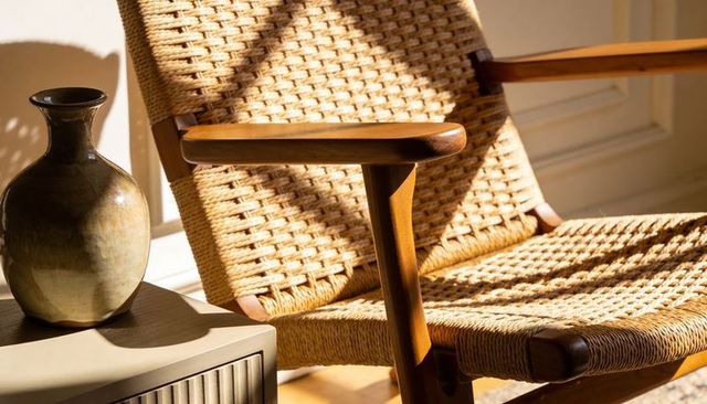 Mid-century woven lounge chair basking in warm sunlight with ceramic vase and timber texture