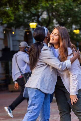 African american female friends hugging on urban plaza at dusk, smiling greeting moment
