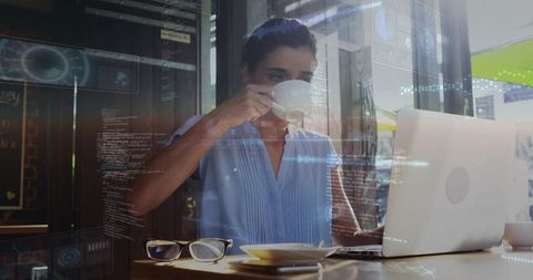 Professional working on laptop in cafe drinking coffee with holographic data overlay