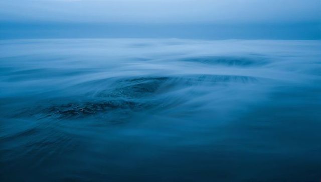 Minimalist silky blue seascape with submerged rock creating flowing water motion tranquil