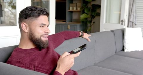 Happy Man Relaxing on Sofa with Smartphone in Hand